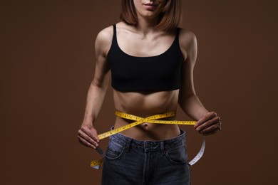 Photo of Anorexic woman measuring her waist on brown background, closeup
