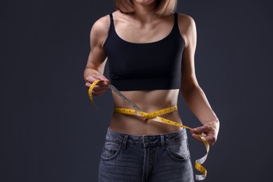 Photo of Anorexic woman measuring her waist on grey background, closeup
