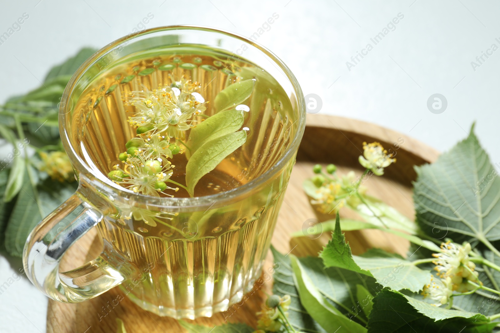 Tasty linden tea in cup, leaves and flowers on light table, closeup Photo of Tasty linden tea in cup, leaves and flowers on light table, closeup