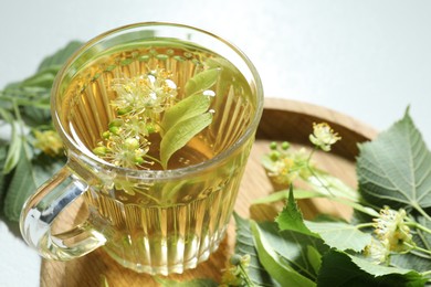 Photo of Tasty linden tea in cup, leaves and flowers on light table, closeup