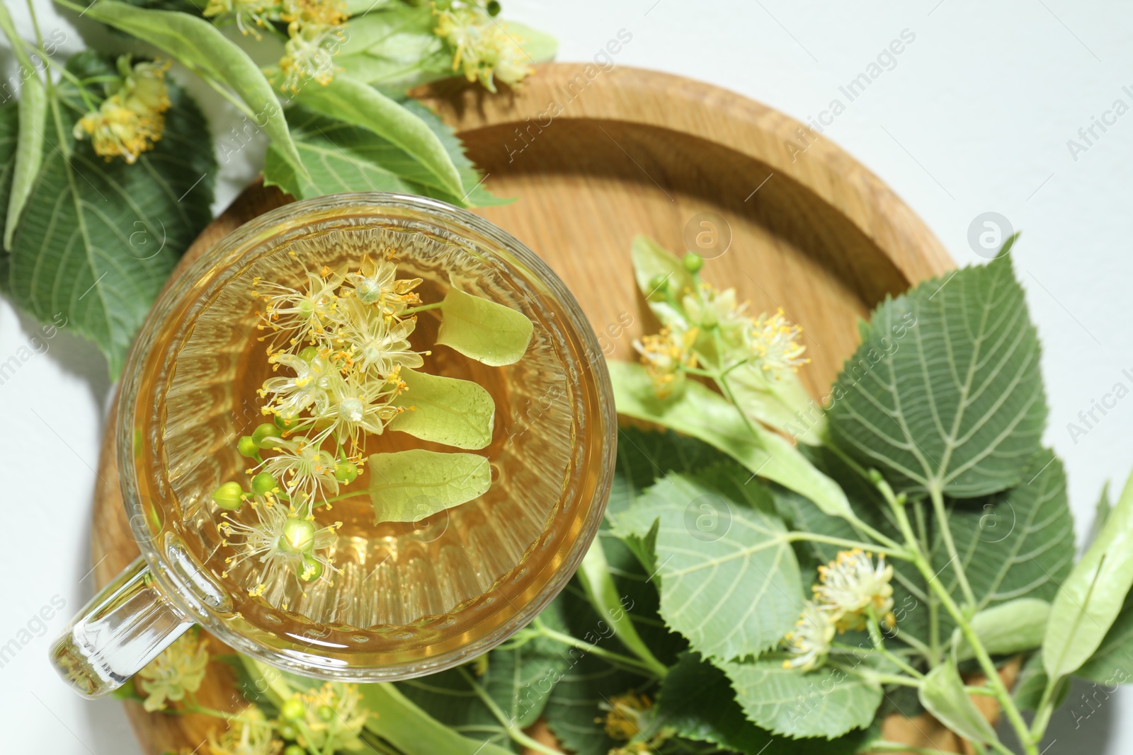 Tasty linden tea in cup, leaves and flowers on light table, flat lay Photo of Tasty linden tea in cup, leaves and flowers on light table, flat lay