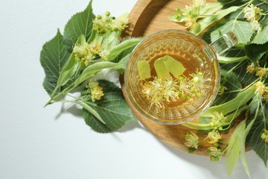 Photo of Tasty linden tea in cup, leaves and flowers on light table, flat lay