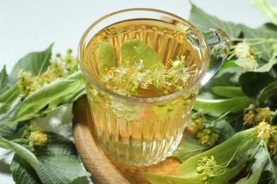 Photo of Tasty linden tea in cup, leaves and flowers on light table, closeup