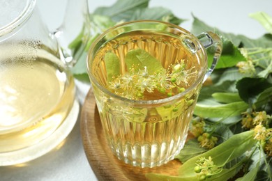 Photo of Tasty linden tea, leaves and flowers on light table, closeup