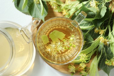 Photo of Tasty linden tea, leaves and flowers on light table, flat lay