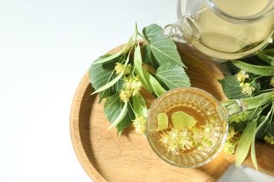 Photo of Tasty linden tea, leaves and flowers on light table, flat lay
