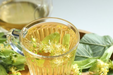 Photo of Tasty linden tea in cup, leaves and flowers on light table, closeup