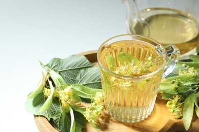 Photo of Tasty linden tea in cup, leaves and flowers on light table, closeup