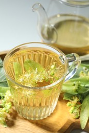 Photo of Tasty linden tea in cup, leaves and flowers on light table, closeup