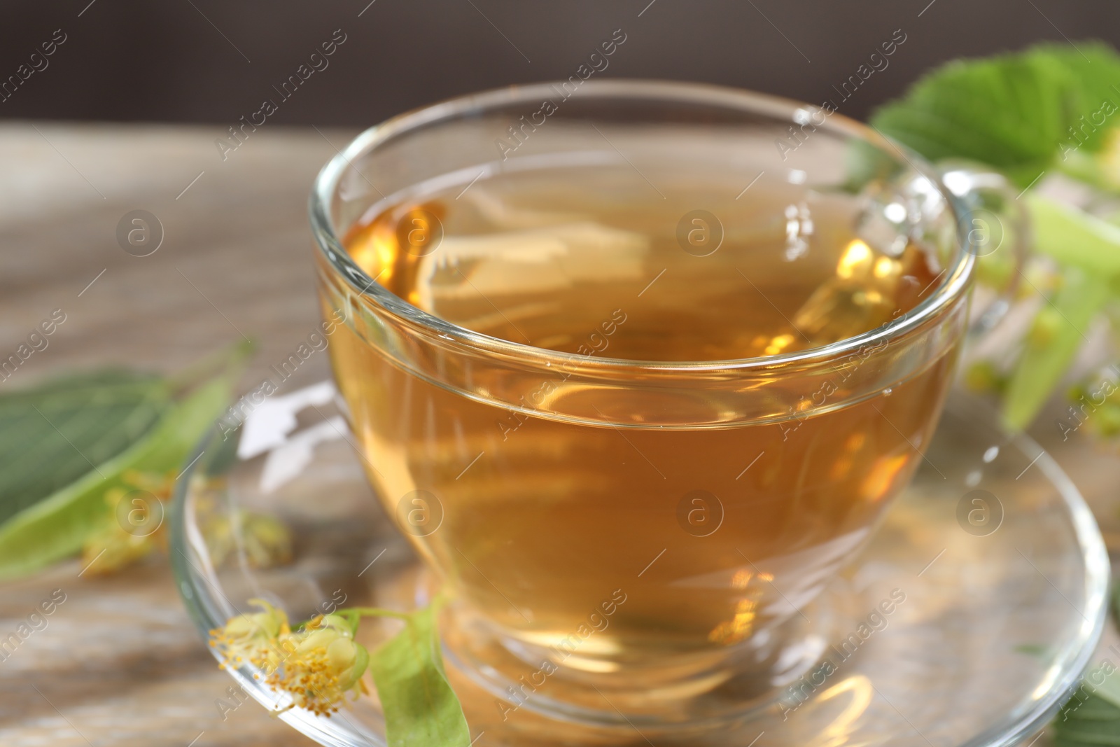 Tasty linden tea in cup, leaves and flowers on wooden table against grey background, closeup Photo of Tasty linden tea in cup, leaves and flowers on wooden table against grey background, closeup