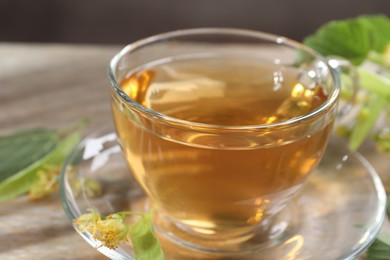 Photo of Tasty linden tea in cup, leaves and flowers on wooden table against grey background, closeup