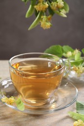 Photo of Tasty linden tea in cup, leaves and flowers on wooden table against grey background, closeup