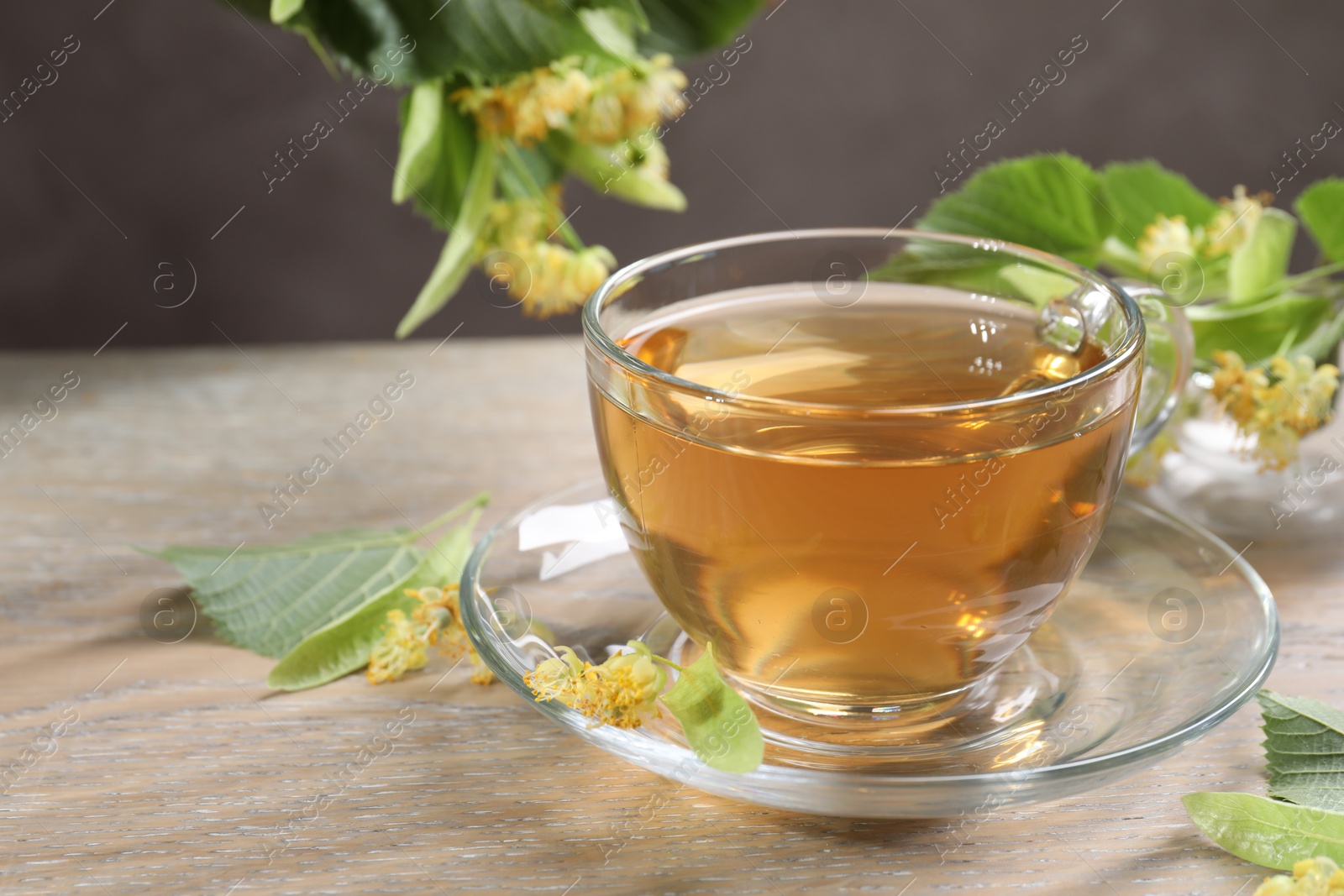 Tasty linden tea in cup, leaves and flowers on wooden table against grey background, closeup Photo of Tasty linden tea in cup, leaves and flowers on wooden table against grey background, closeup