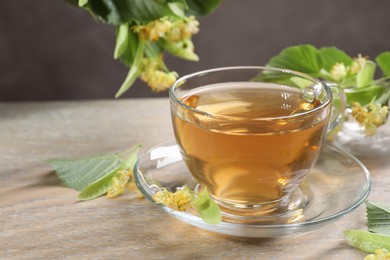 Photo of Tasty linden tea in cup, leaves and flowers on wooden table against grey background, closeup