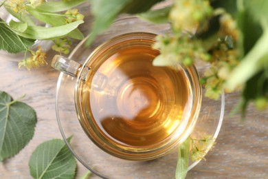 Photo of Tasty linden tea in cup, leaves and flowers on wooden table, flat lay