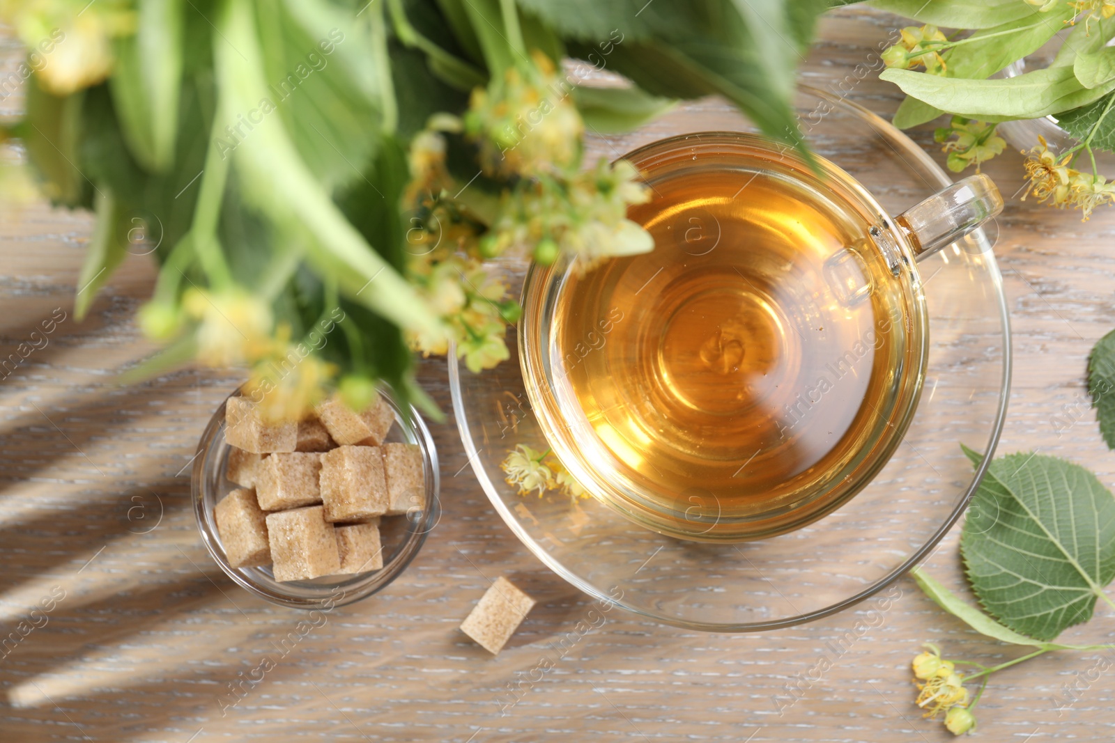 Tasty linden tea in cup, sugar cubes, leaves and flowers on wooden table, flat lay Photo of Tasty linden tea in cup, sugar cubes, leaves and flowers on wooden table, flat lay