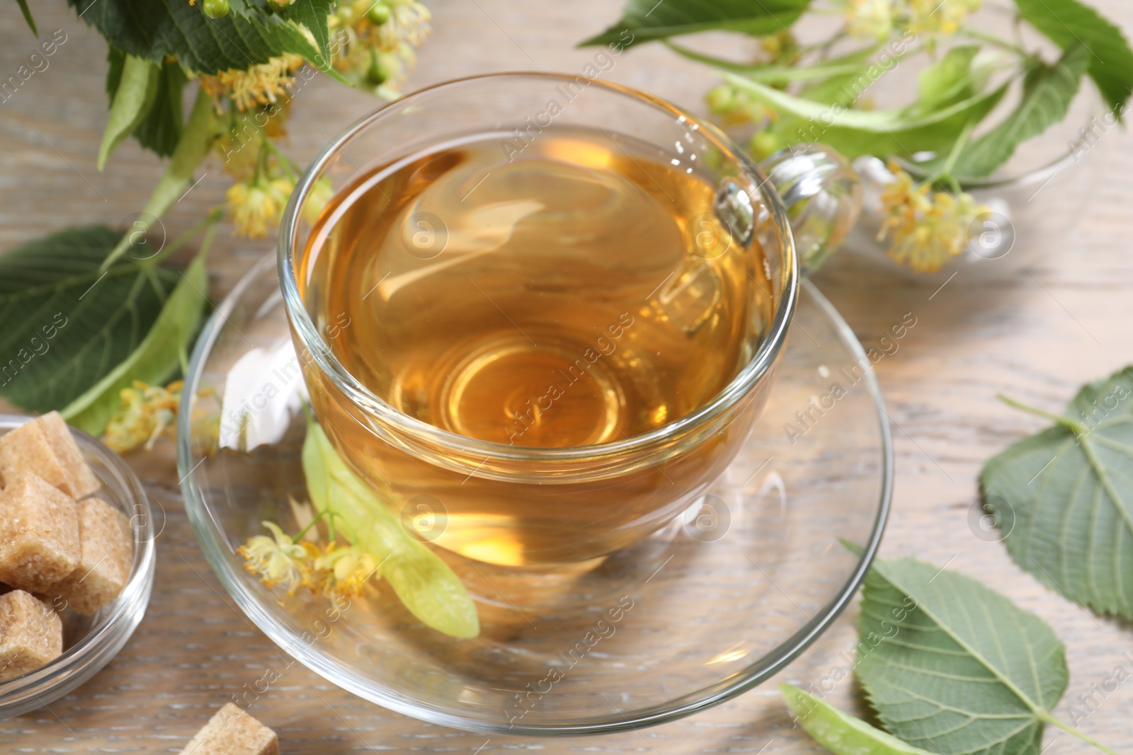 Tasty linden tea in cup, sugar cubes, leaves and flowers on wooden table, closeup Photo of Tasty linden tea in cup, sugar cubes, leaves and flowers on wooden table, closeup