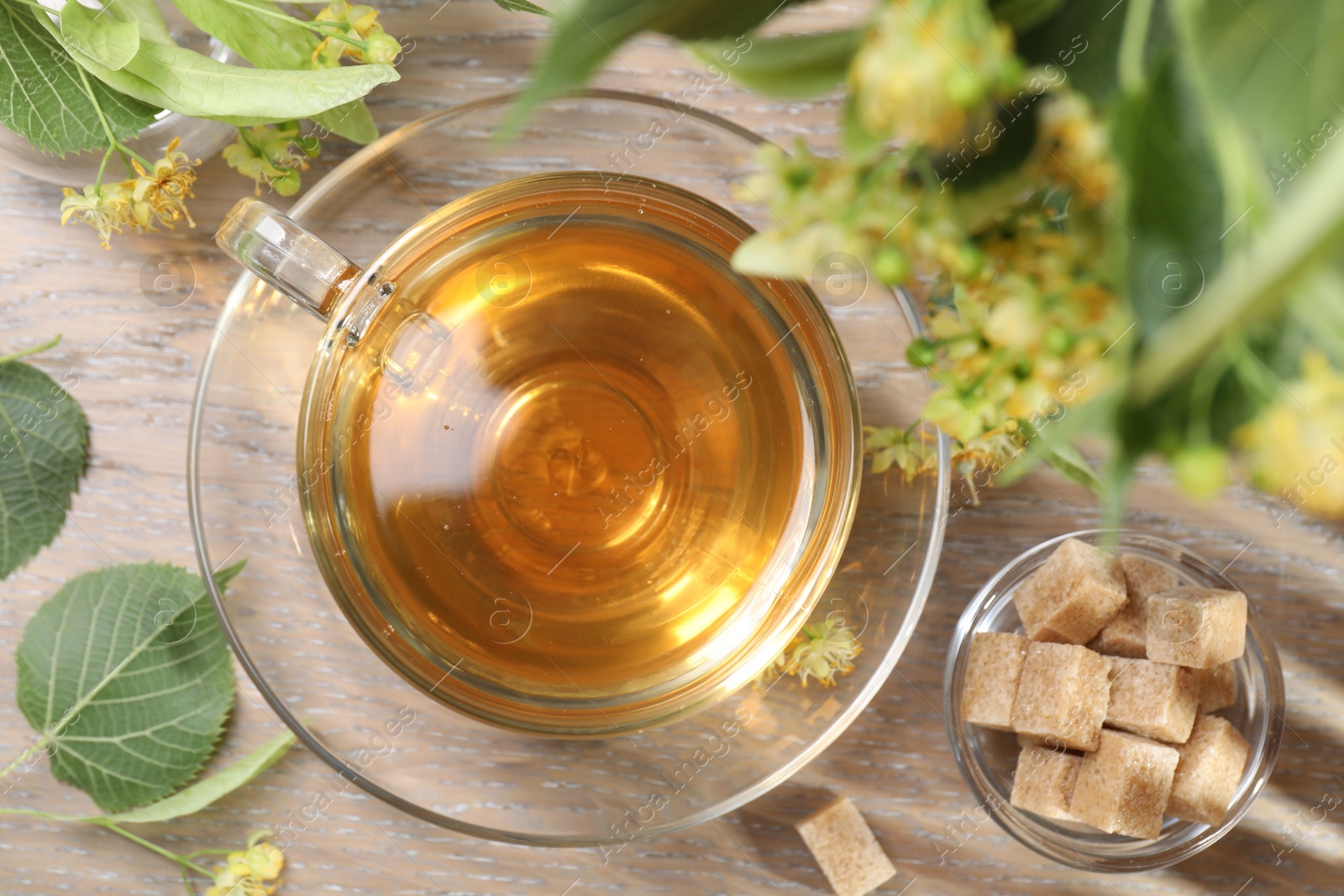 Tasty linden tea in cup, sugar cubes, leaves and flowers on wooden table, flat lay Photo of Tasty linden tea in cup, sugar cubes, leaves and flowers on wooden table, flat lay
