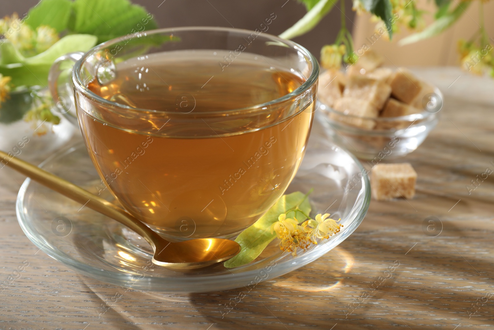 Tasty linden tea in cup, spoon, leaves and flowers on wooden table, closeup Photo of Tasty linden tea in cup, spoon, leaves and flowers on wooden table, closeup
