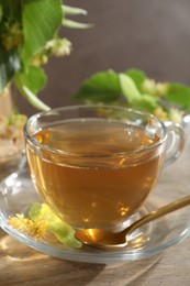 Photo of Tasty linden tea in cup, spoon, leaves and flowers on wooden table against grey background, closeup