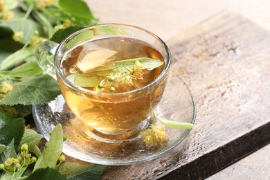 Photo of Tasty linden tea in cup, leaves and flowers on table, closeup