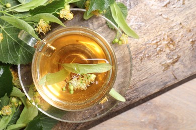 Photo of Tasty linden tea in cup, leaves and flowers on wooden table, top view