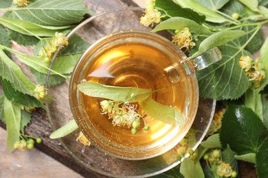 Photo of Tasty linden tea in cup, leaves and flowers on wooden table, top view