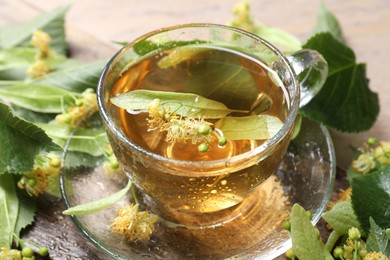 Photo of Tasty linden tea in cup, leaves and flowers on table, closeup