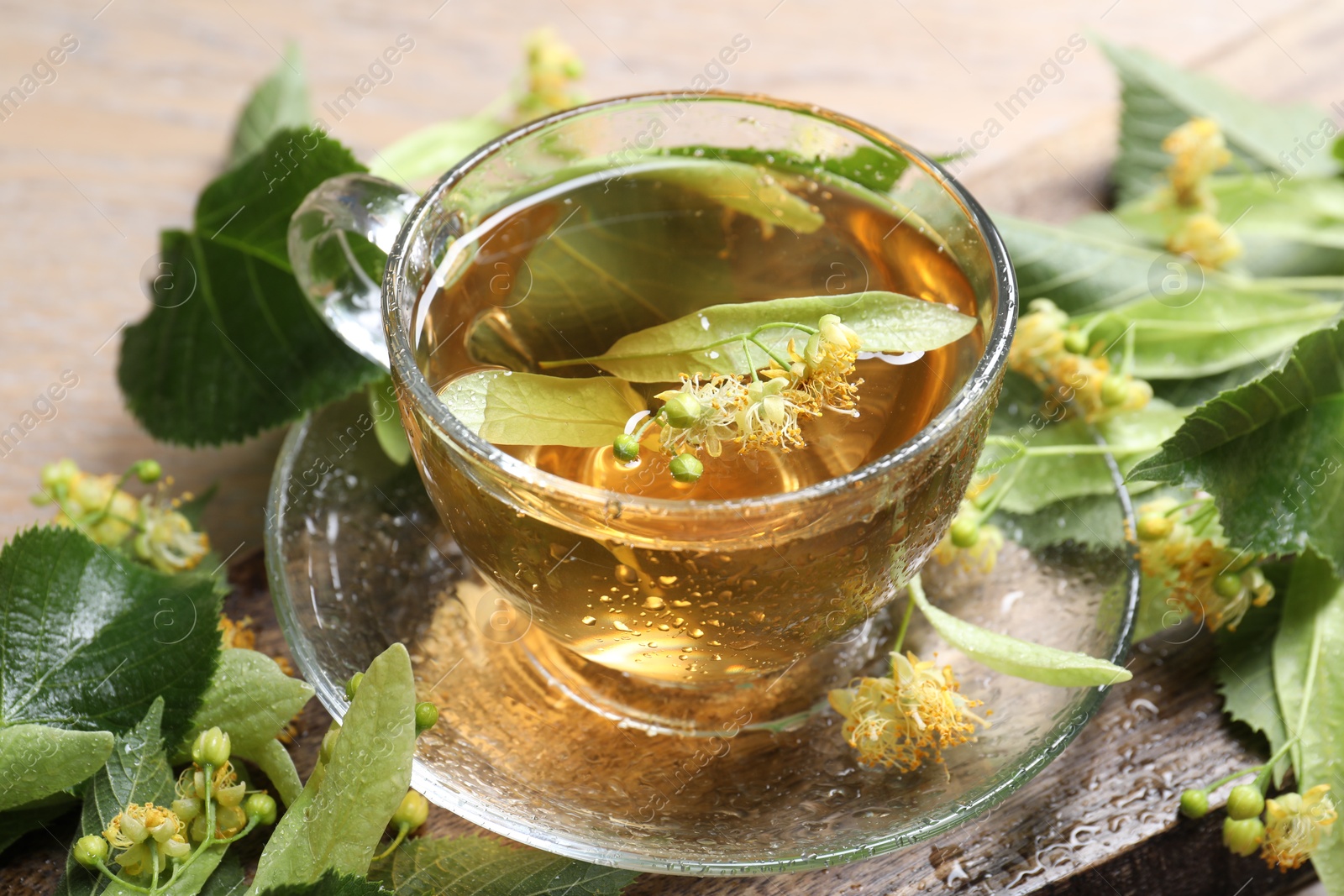 Tasty linden tea in cup, leaves and flowers on table, closeup Photo of Tasty linden tea in cup, leaves and flowers on table, closeup