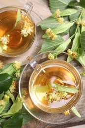 Photo of Tasty linden tea in cups, leaves and flowers on wooden table, flat lay