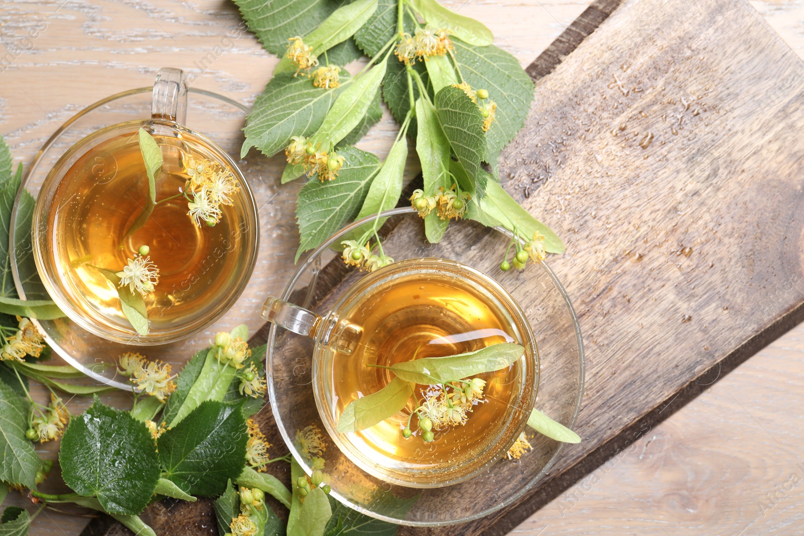 Tasty linden tea in cups, leaves and flowers on wooden table, flat lay Photo of Tasty linden tea in cups, leaves and flowers on wooden table, flat lay