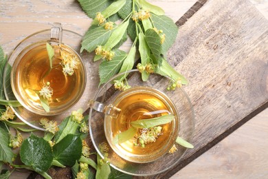 Photo of Tasty linden tea in cups, leaves and flowers on wooden table, flat lay