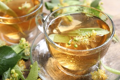 Photo of Tasty linden tea in cups, leaves and flowers on table, closeup