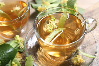 Photo of Tasty linden tea in cups, leaves and flowers on wooden table, closeup