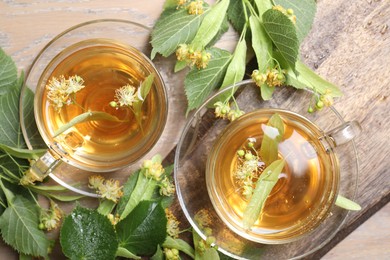 Photo of Tasty linden tea in cups, leaves and flowers on wooden table, flat lay