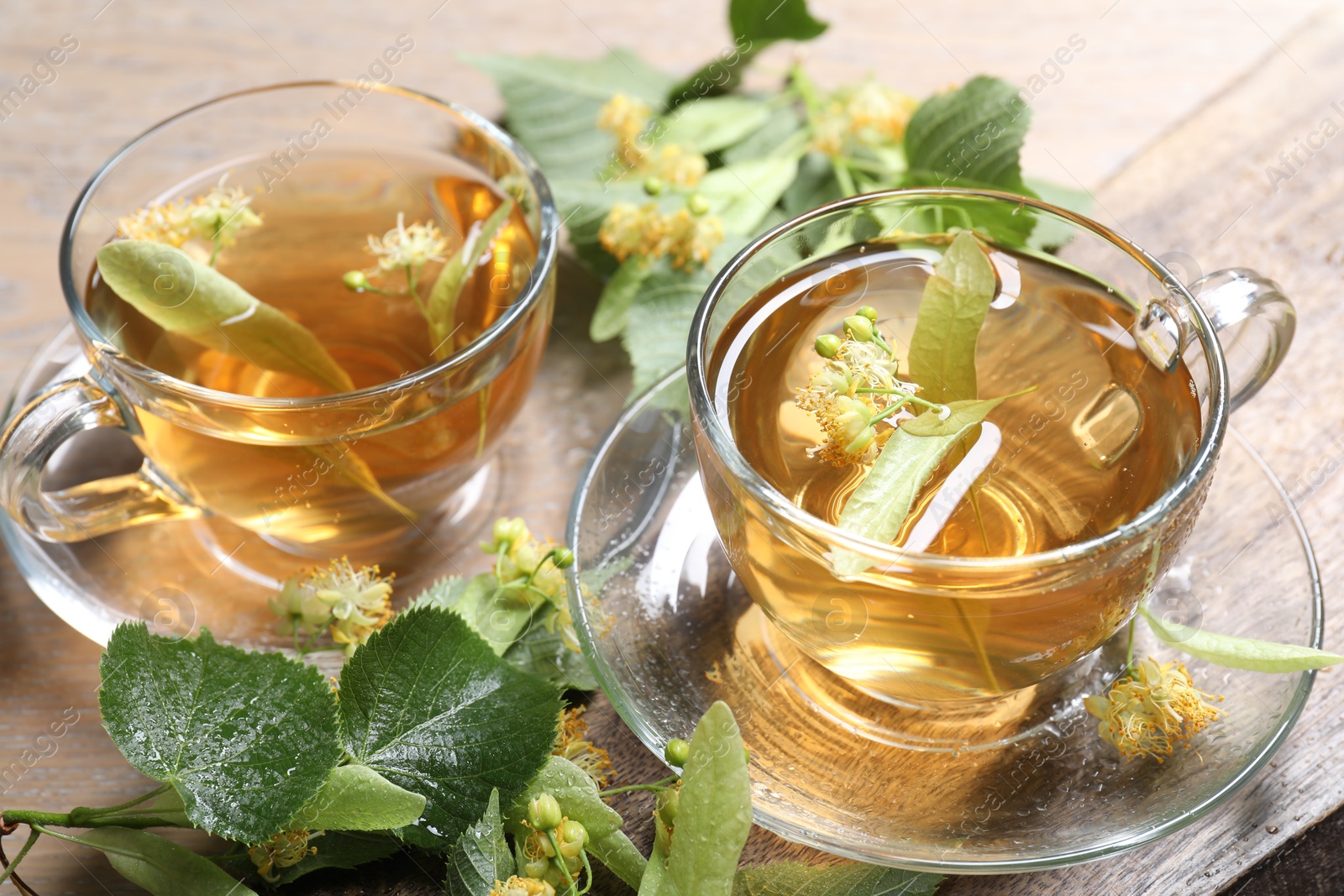 Tasty linden tea in cups, leaves and flowers on wooden table, closeup Photo of Tasty linden tea in cups, leaves and flowers on wooden table, closeup