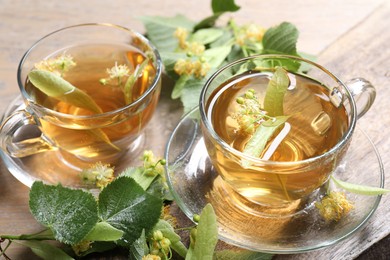 Photo of Tasty linden tea in cups, leaves and flowers on wooden table, closeup