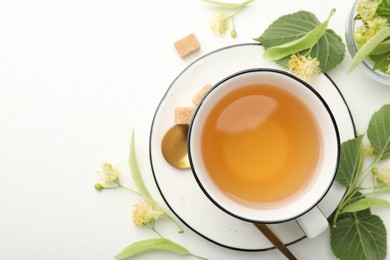 Photo of Tasty linden tea in cup, spoon, sugar cubes, leaves and flowers on white table, flat lay. Space for text