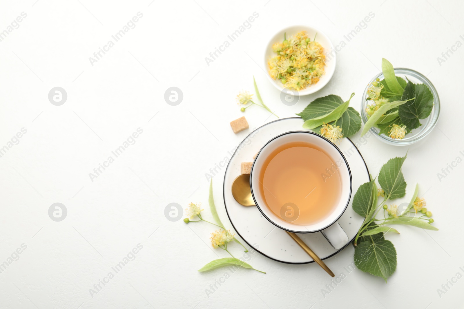 Tasty linden tea in cup, spoon, sugar cubes, leaves and flowers on white table, flat lay. Space for text Photo of Tasty linden tea in cup, spoon, sugar cubes, leaves and flowers on white table, flat lay. Space for text