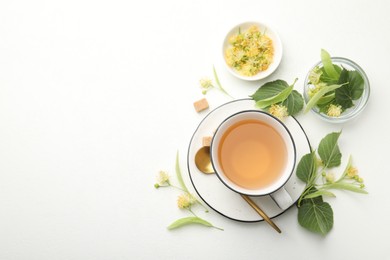 Photo of Tasty linden tea in cup, spoon, sugar cubes, leaves and flowers on white table, flat lay. Space for text