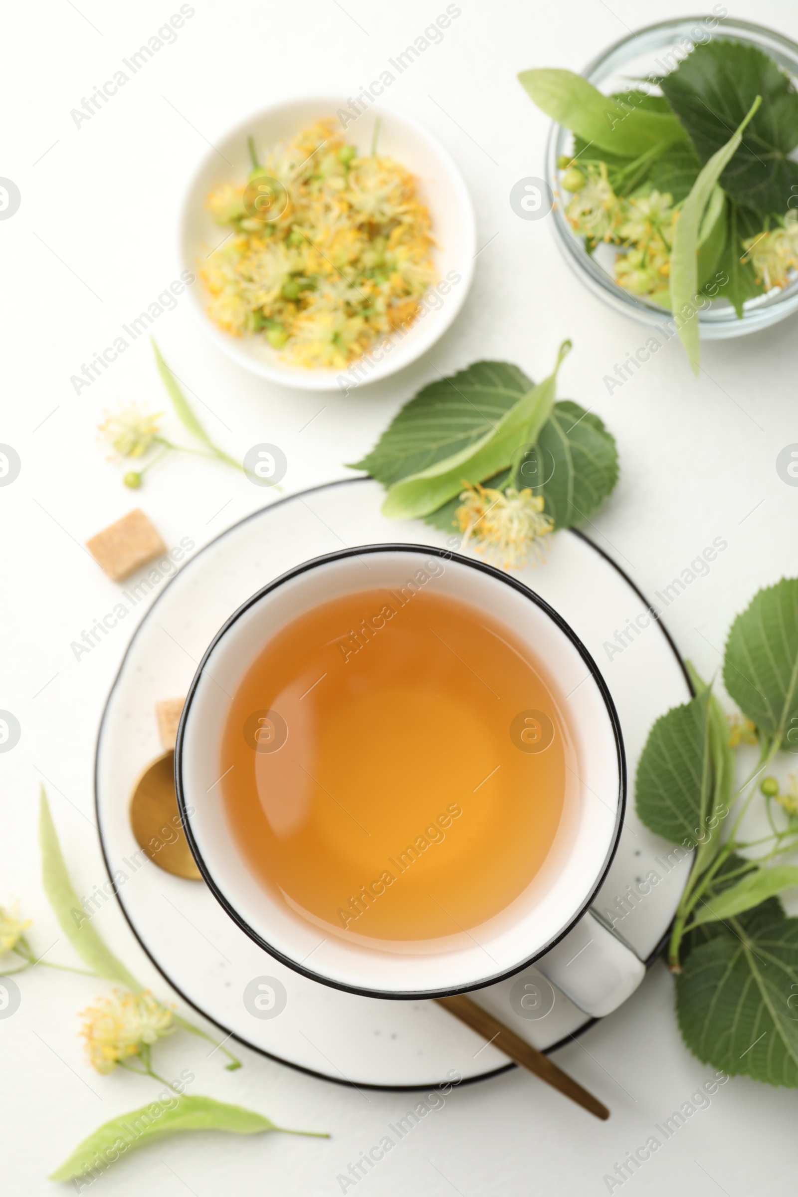 Tasty linden tea in cup, spoon, sugar cubes, leaves and flowers on white table, flat lay Photo of Tasty linden tea in cup, spoon, sugar cubes, leaves and flowers on white table, flat lay