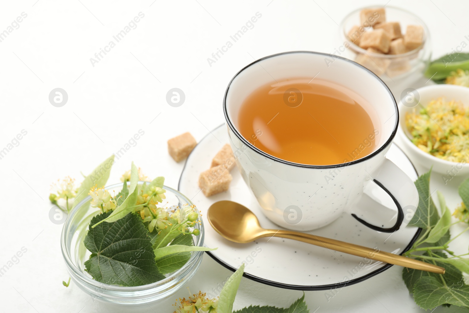 Tasty linden tea in cup, spoon, sugar cubes, leaves and flowers on white table, closeup Photo of Tasty linden tea in cup, spoon, sugar cubes, leaves and flowers on white table, closeup