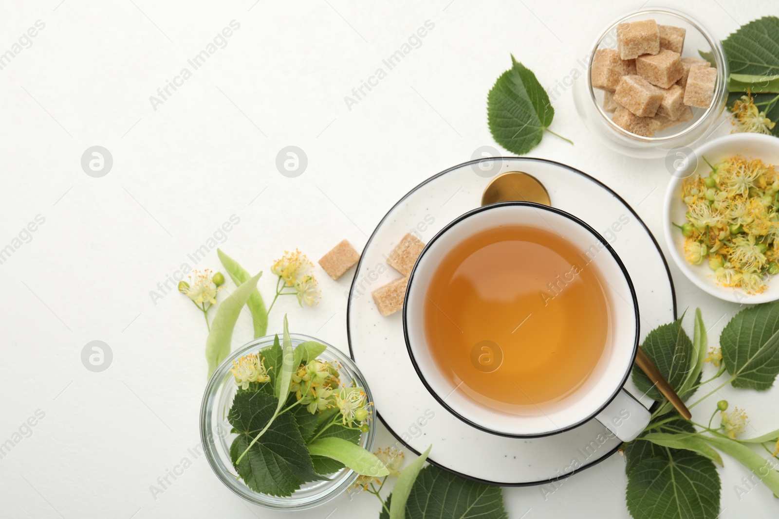 Tasty linden tea in cup, sugar cubes, leaves and flowers on white table, flat lay. Space for text Photo of Tasty linden tea in cup, sugar cubes, leaves and flowers on white table, flat lay. Space for text