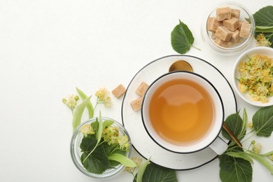 Photo of Tasty linden tea in cup, sugar cubes, leaves and flowers on white table, flat lay. Space for text