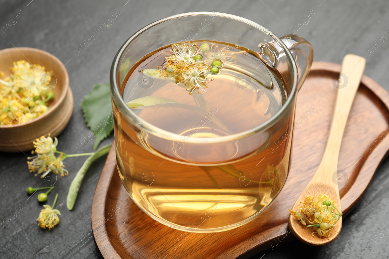 Tasty linden tea in cup, spoon, leaves and flowers on dark textured table, closeup Photo of Tasty linden tea in cup, spoon, leaves and flowers on dark textured table, closeup