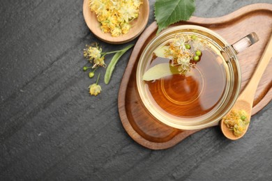 Photo of Tasty linden tea in cup, spoon, leaves and flowers on dark textured table, flat lay. Space for text
