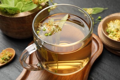 Photo of Tasty linden tea in cup, leaves and flowers on dark textured table, closeup