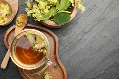 Photo of Tasty linden tea in cup, spoon, leaves and flowers on dark textured table, flat lay. Space for text
