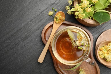 Photo of Tasty linden tea in cup, spoon, leaves and flowers on dark textured table, flat lay. Space for text