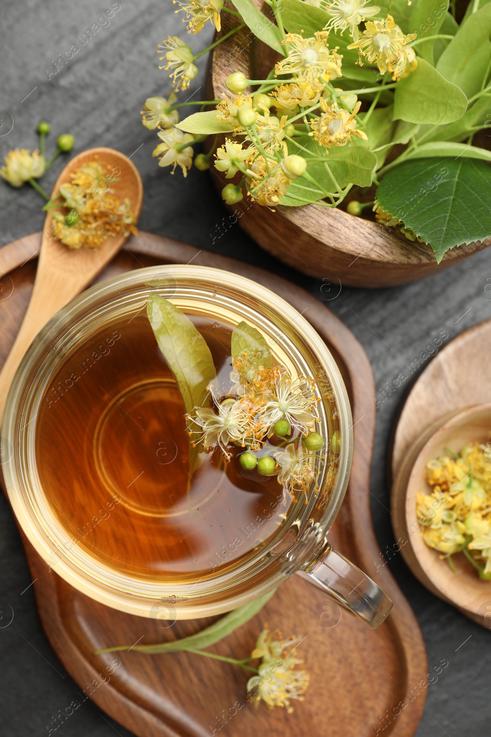 Tasty linden tea in cup, spoon, leaves and flowers on dark textured table, flat lay Photo of Tasty linden tea in cup, spoon, leaves and flowers on dark textured table, flat lay